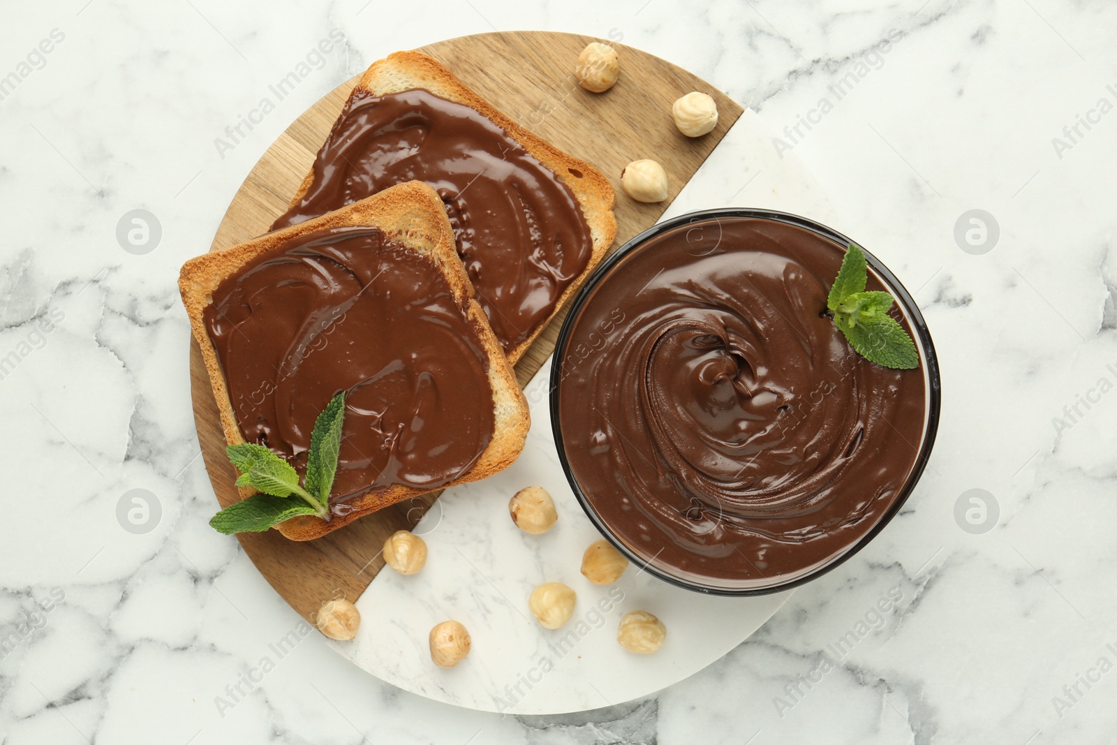 Tasty chocolate spread with mint and hazelnuts on white marble table, top view Photo of Tasty chocolate spread with mint and hazelnuts on white marble table, top view