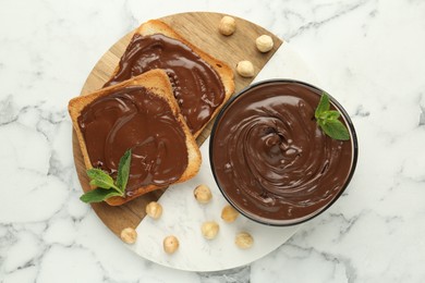 Photo of Tasty chocolate spread with mint and hazelnuts on white marble table, top view