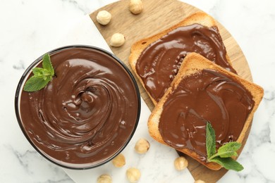 Photo of Tasty chocolate spread with mint and hazelnuts on white marble table, top view
