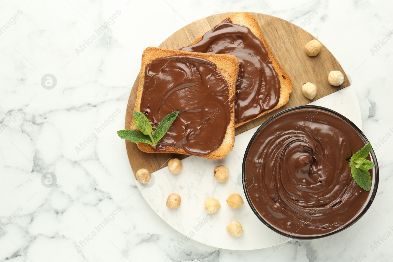 Tasty chocolate spread with mint and hazelnuts on white marble table, top view Photo of Tasty chocolate spread with mint and hazelnuts on white marble table, top view