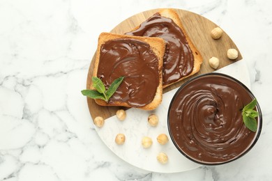 Photo of Tasty chocolate spread with mint and hazelnuts on white marble table, top view