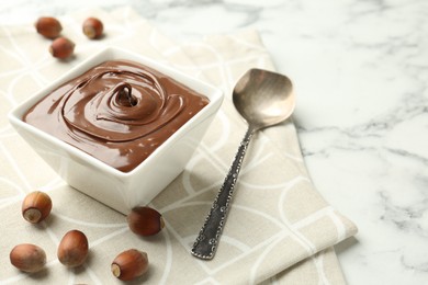 Photo of Tasty chocolate spread and hazelnuts on table, closeup