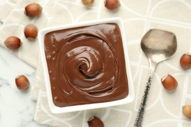 Photo of Tasty chocolate spread and hazelnuts on white table, flat lay