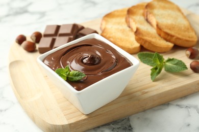 Photo of Tasty chocolate spread, pieces, toasts, mint and hazelnuts on white marble table, closeup