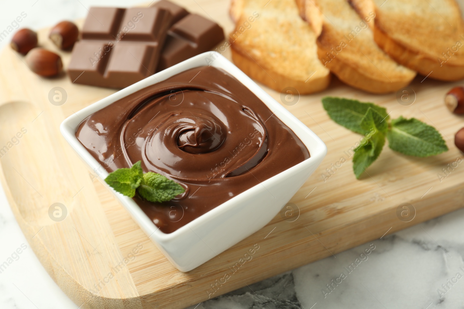 Tasty chocolate spread, pieces, toasts, mint and hazelnuts on white marble table, closeup Photo of Tasty chocolate spread, pieces, toasts, mint and hazelnuts on white marble table, closeup
