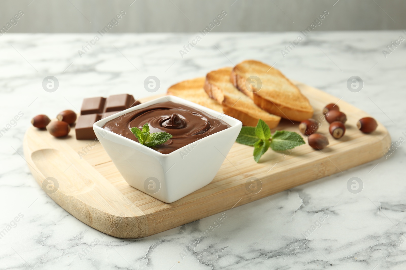 Tasty chocolate spread, pieces, toasts, mint and hazelnuts on white marble table, closeup Photo of Tasty chocolate spread, pieces, toasts, mint and hazelnuts on white marble table, closeup