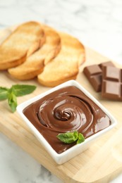 Photo of Tasty chocolate spread, pieces, toasts, mint and hazelnuts on white marble table, closeup