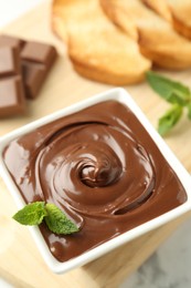Photo of Tasty chocolate spread, pieces, toasts, mint and hazelnuts on white table, closeup