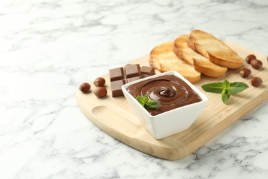 Photo of Tasty chocolate spread, pieces, toasts, mint and hazelnuts on white marble table. Space for text