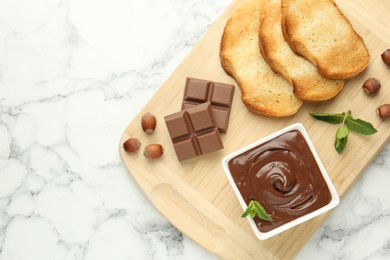 Photo of Tasty chocolate spread, pieces, toasts, mint and hazelnuts on white marble table, top view. Space for text