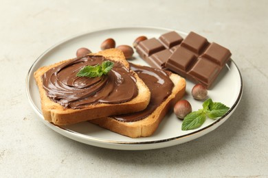 Photo of Toasts with tasty chocolate spread, pieces, mint and hazelnuts on light table, closeup