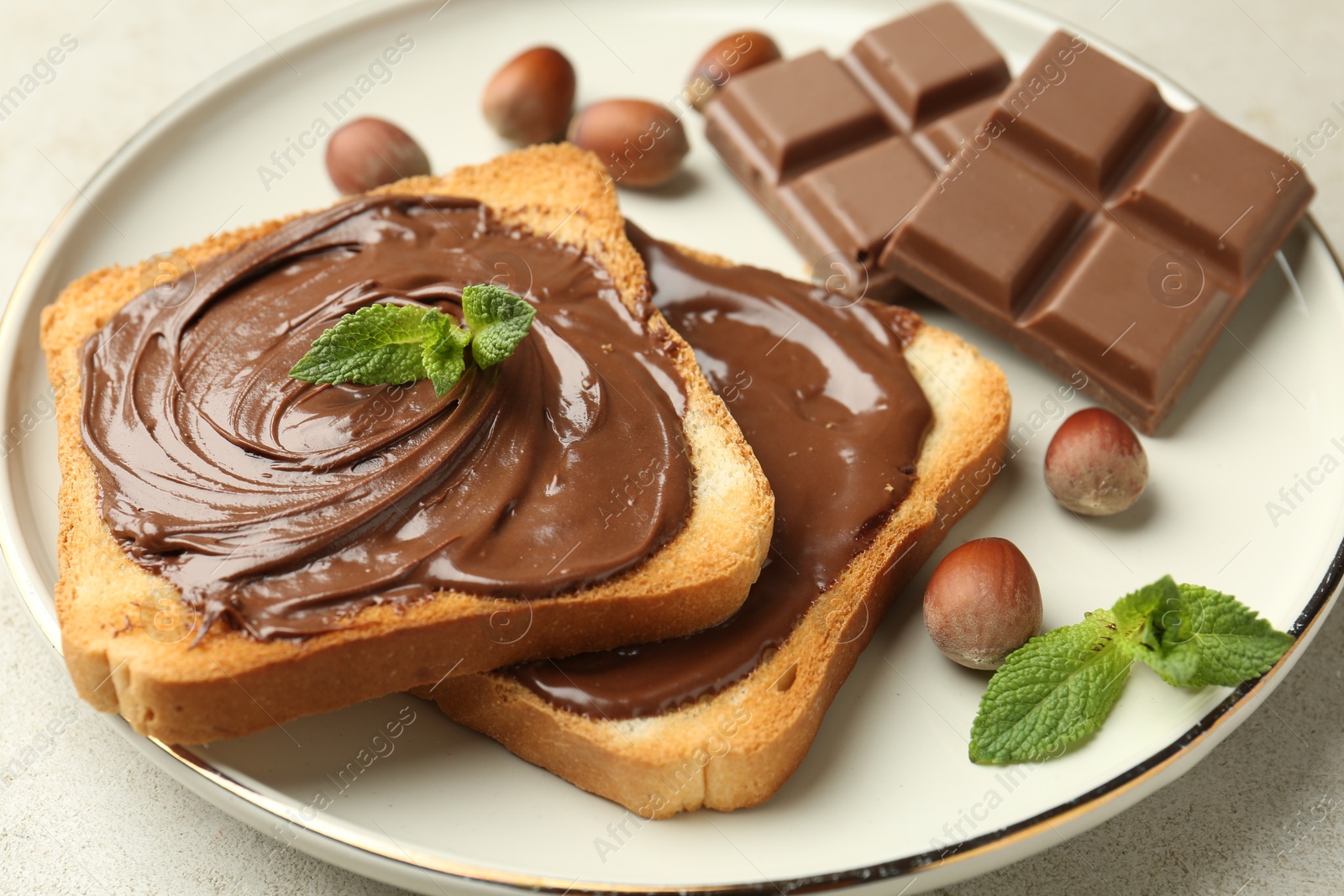 Toasts with tasty chocolate spread, pieces, mint and hazelnuts on light table, closeup Photo of Toasts with tasty chocolate spread, pieces, mint and hazelnuts on light table, closeup