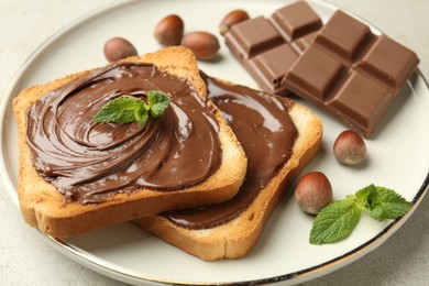 Photo of Toasts with tasty chocolate spread, pieces, mint and hazelnuts on light table, closeup