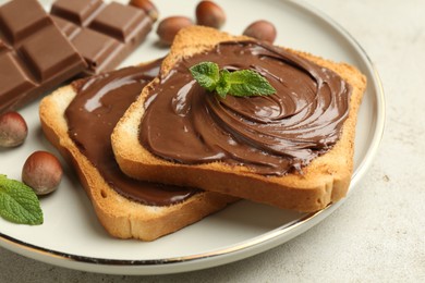 Photo of Toasts with tasty chocolate spread, pieces, mint and hazelnuts on light table, closeup
