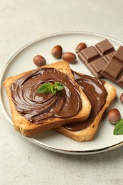 Photo of Toasts with tasty chocolate spread, pieces, mint and hazelnuts on light table, closeup