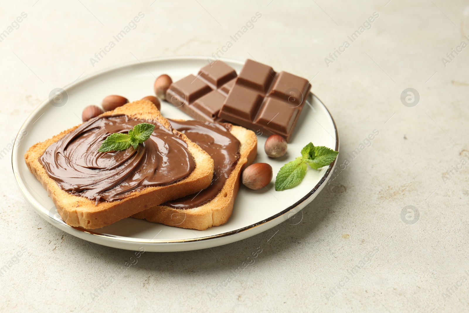 Photo of Toasts with tasty chocolate spread, pieces, mint and hazelnuts on light table, closeup