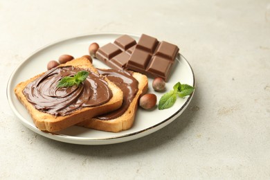 Photo of Toasts with tasty chocolate spread, pieces, mint and hazelnuts on light table, closeup