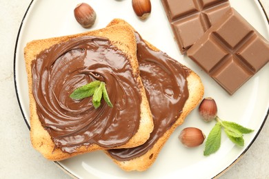 Photo of Toasts with tasty chocolate spread, pieces, mint and hazelnuts on light table, top view