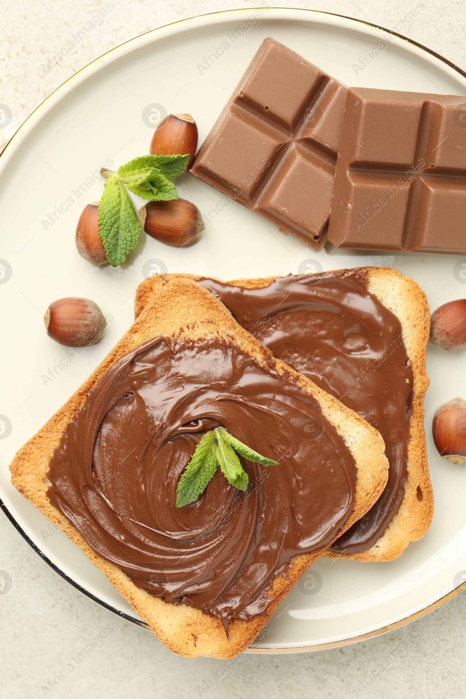 Toasts with tasty chocolate spread, pieces, mint and hazelnuts on light table, top view Photo of Toasts with tasty chocolate spread, pieces, mint and hazelnuts on light table, top view