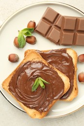 Photo of Toasts with tasty chocolate spread, pieces, mint and hazelnuts on light table, top view