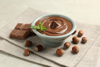 Photo of Tasty chocolate spread, pieces, mint and hazelnuts on light table, closeup