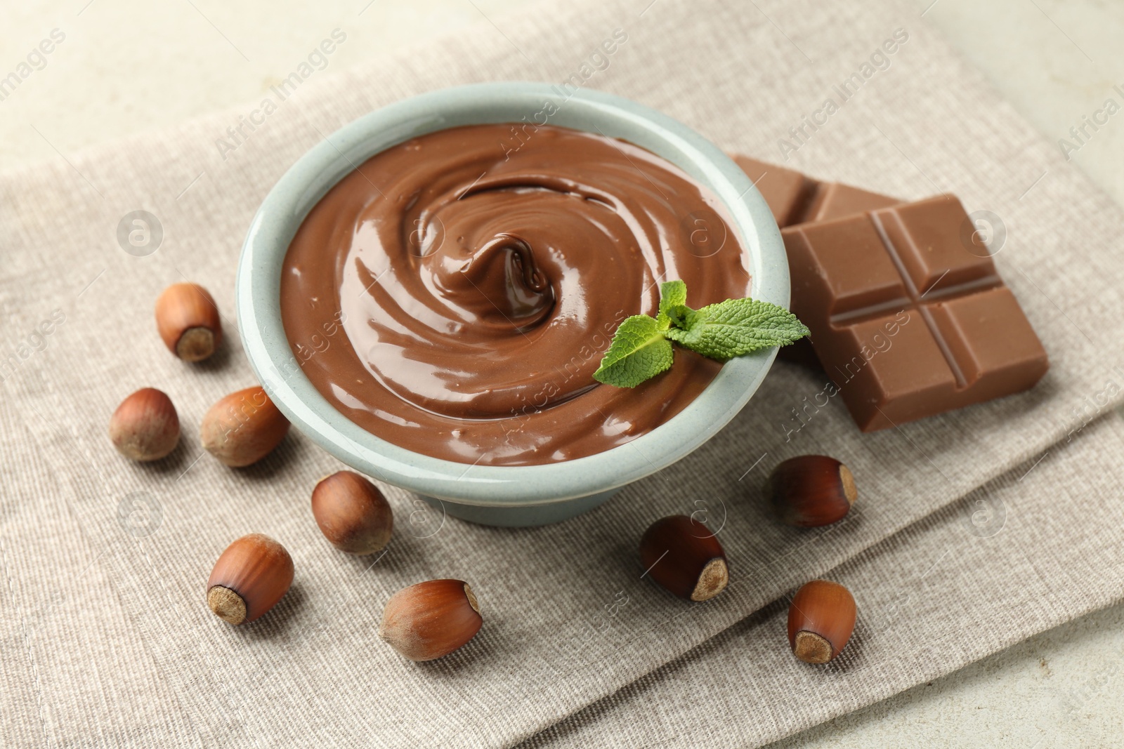 Tasty chocolate spread, pieces, mint and hazelnuts on light table, closeup Photo of Tasty chocolate spread, pieces, mint and hazelnuts on light table, closeup