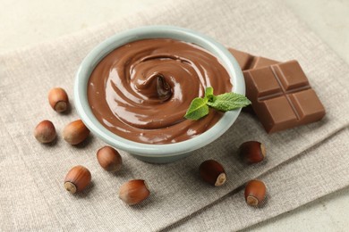 Photo of Tasty chocolate spread, pieces, mint and hazelnuts on light table, closeup