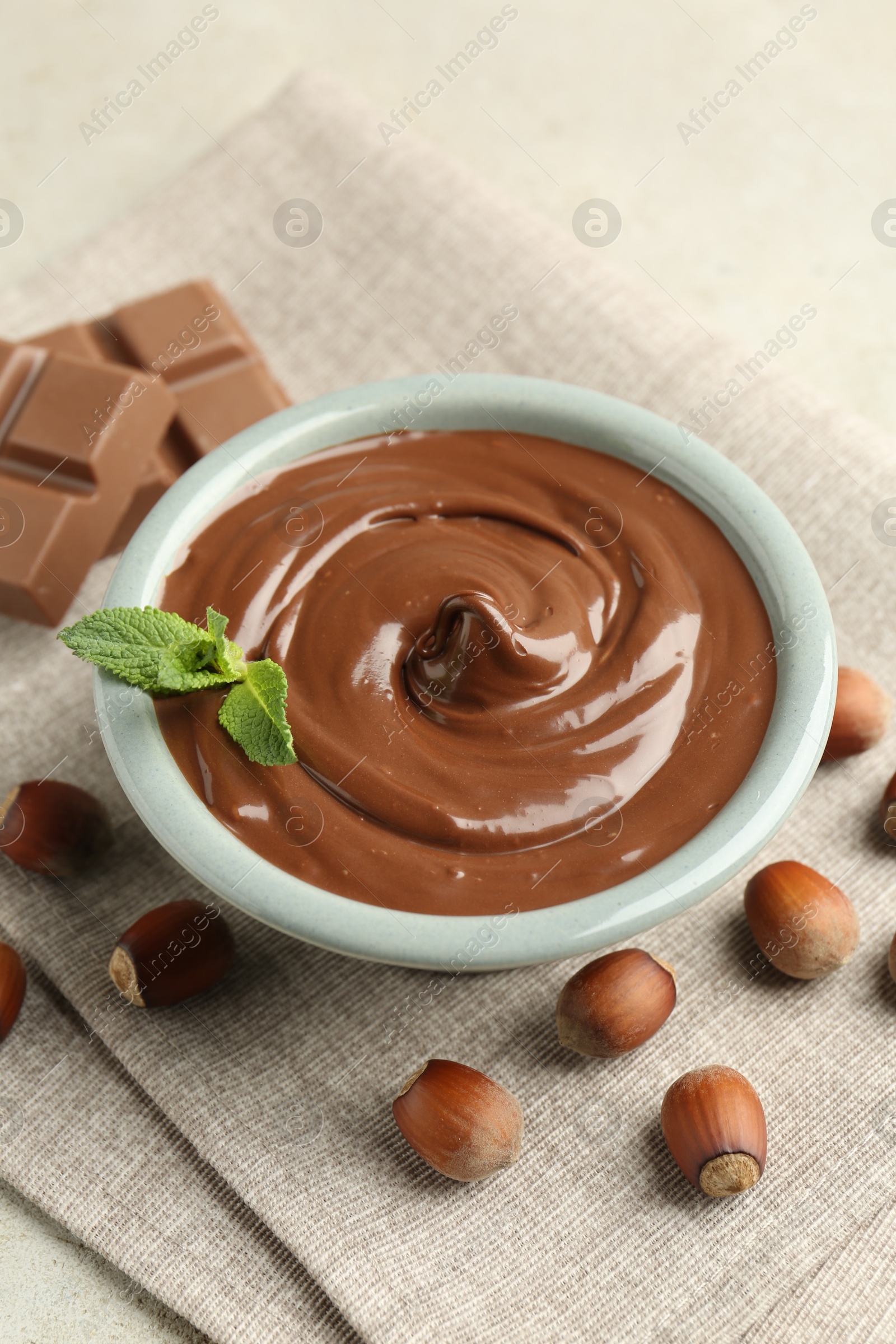Tasty chocolate spread, pieces, mint and hazelnuts on light table, closeup Photo of Tasty chocolate spread, pieces, mint and hazelnuts on light table, closeup