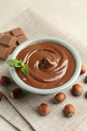 Photo of Tasty chocolate spread, pieces, mint and hazelnuts on light table, closeup