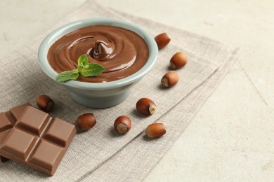 Photo of Tasty chocolate spread, pieces, mint and hazelnuts on light table, closeup
