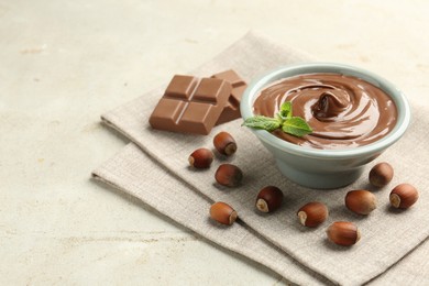 Photo of Tasty chocolate spread, pieces, mint and hazelnuts on light table, closeup. Space for text