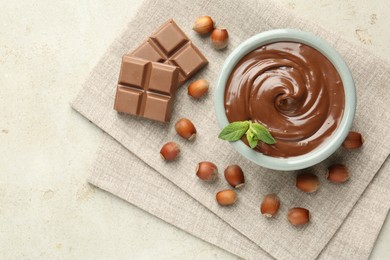 Photo of Tasty chocolate spread, pieces, mint and hazelnuts on light table, flat lay