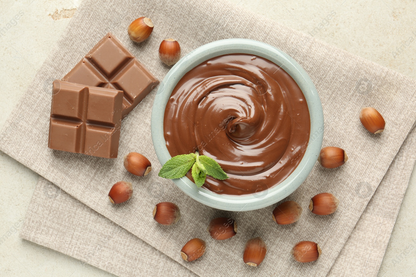 Tasty chocolate spread, pieces, mint and hazelnuts on light table, flat lay Photo of Tasty chocolate spread, pieces, mint and hazelnuts on light table, flat lay