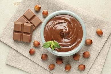 Photo of Tasty chocolate spread, pieces, mint and hazelnuts on light table, flat lay
