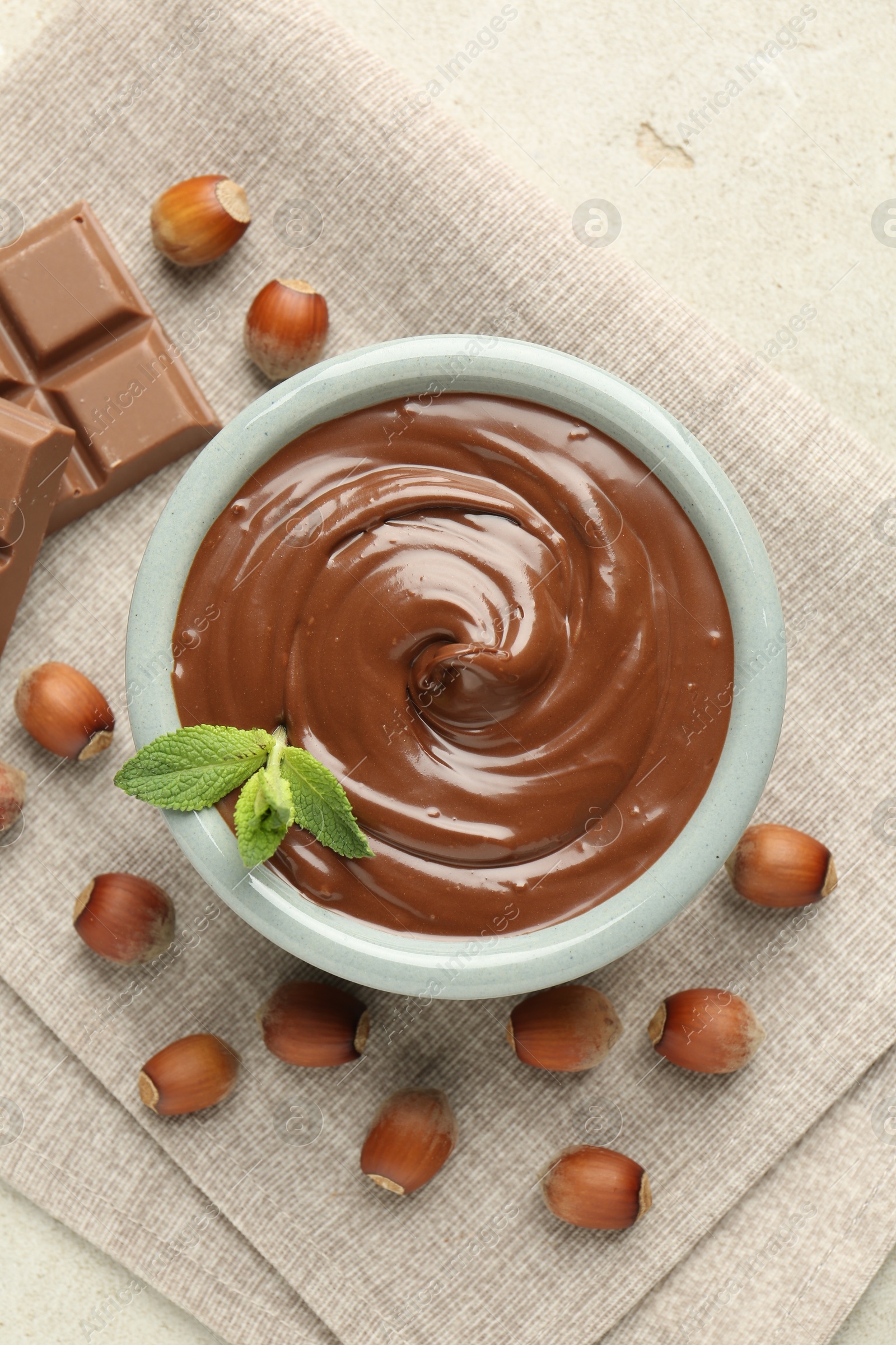 Photo of Tasty chocolate spread, pieces, mint and hazelnuts on light table, flat lay
