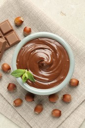 Photo of Tasty chocolate spread, pieces, mint and hazelnuts on light table, flat lay