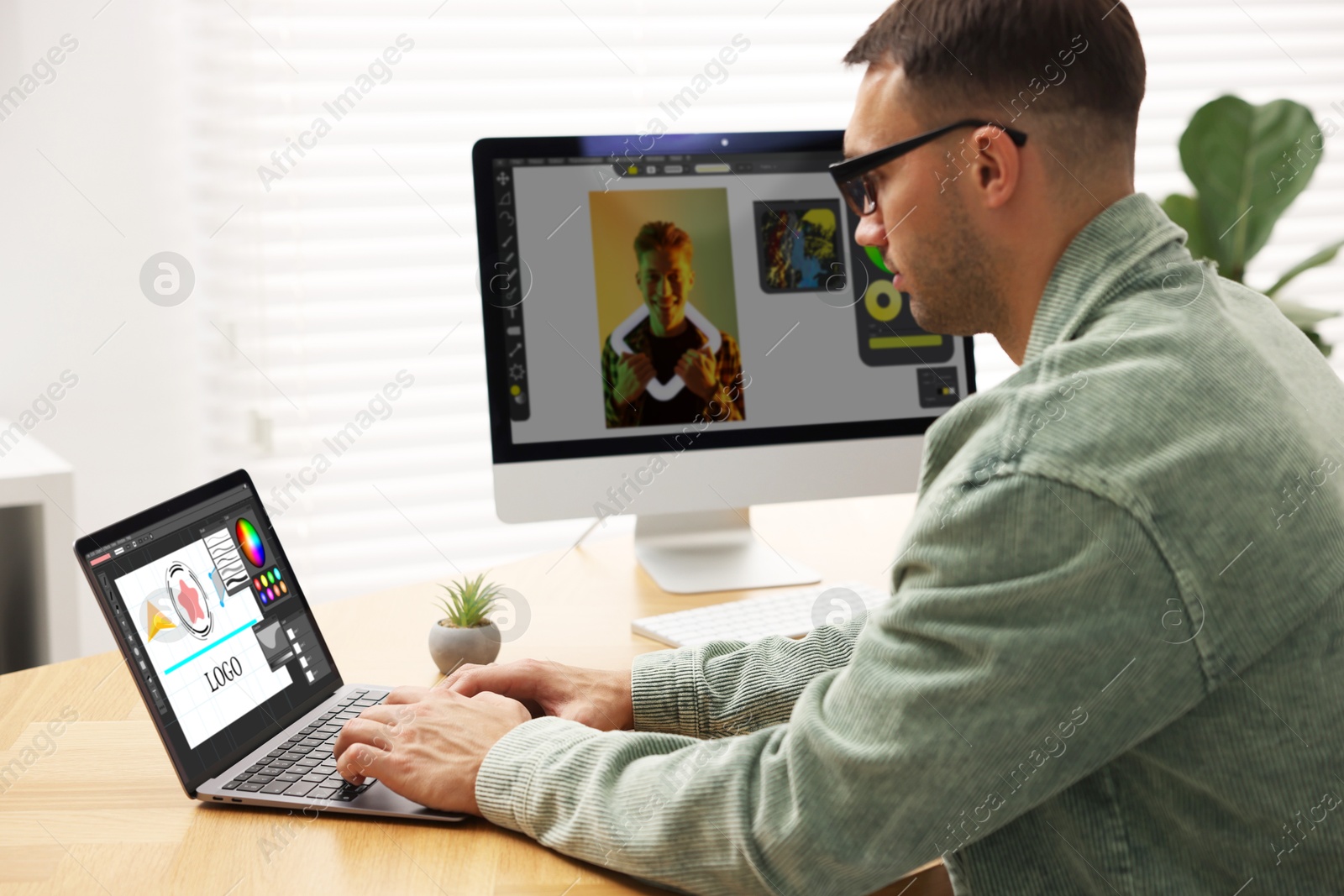 Designer working on different computers at table in office Image of Designer working on different computers at table in office