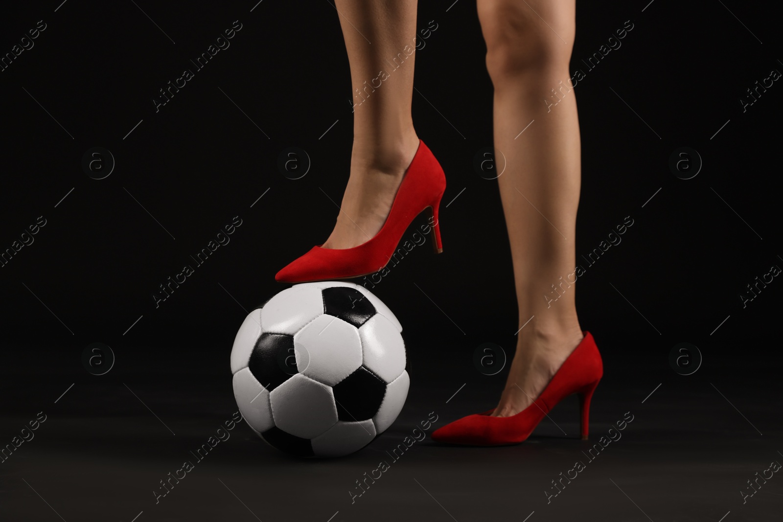 Photo of Woman in high heeled shoes with soccer ball on dark background, closeup