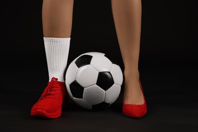 Photo of Woman in high heeled shoe and sneaker with soccer ball on dark background, closeup