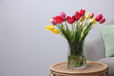 Photo of Bouquet of beautiful tulips on rattan table indoors. Space for text