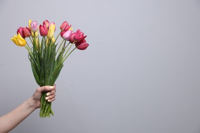 Photo of Woman with bouquet of beautiful tulips on light grey background, closeup. Space for text