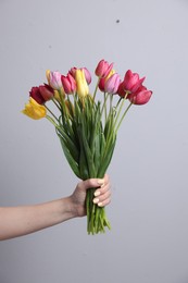 Photo of Woman with bouquet of beautiful tulips on light grey background, closeup