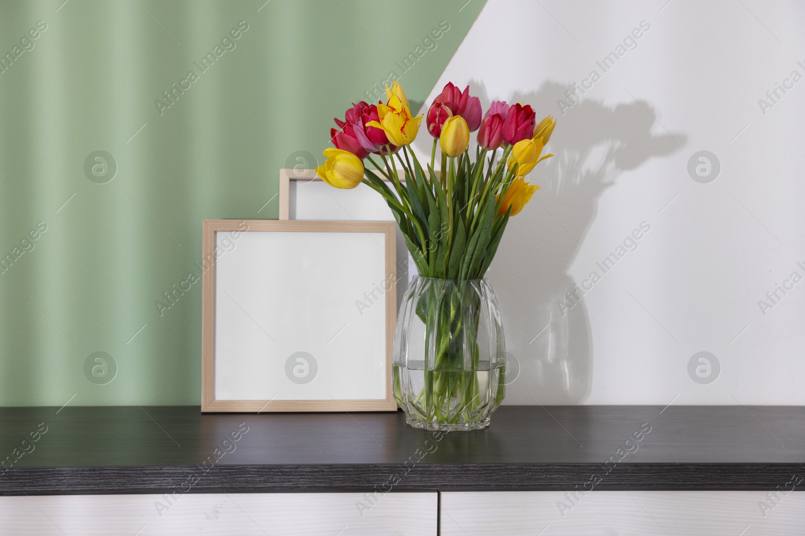 Photo of Bouquet of beautiful tulips and frames on table near color wall