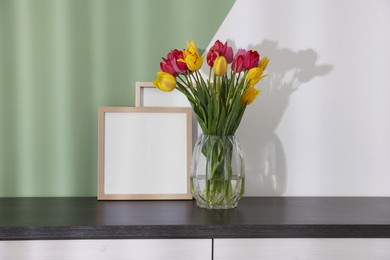 Photo of Bouquet of beautiful tulips and frames on table near color wall