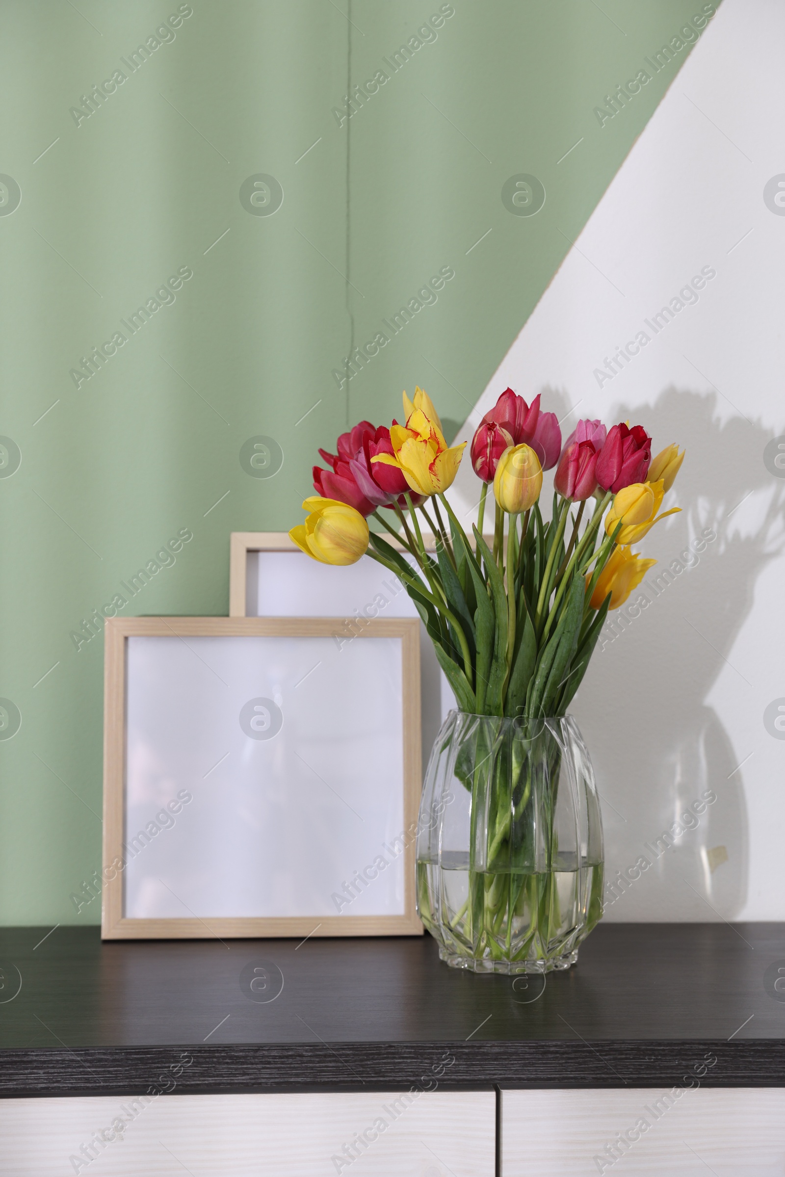 Photo of Bouquet of beautiful tulips and frames on table near color wall
