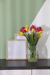 Photo of Bouquet of beautiful tulips and frames on table near color wall