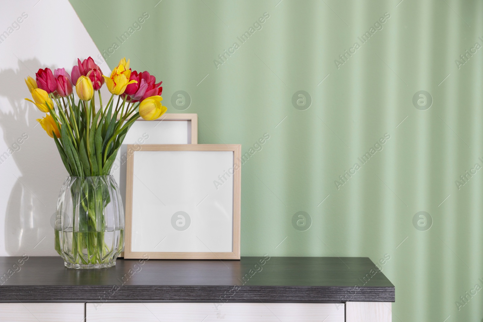 Photo of Bouquet of beautiful tulips and frames on table near color wall. Space for text