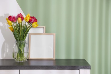 Photo of Bouquet of beautiful tulips and frames on table near color wall. Space for text