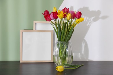 Photo of Bouquet of beautiful tulips and frames on table near color wall