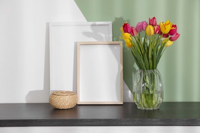 Photo of Bouquet of beautiful tulips and frames on table near color wall